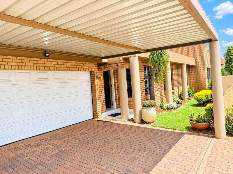 Front exterior view featuring a paved driveway, a covered carport, and a brick facade with a sectional garage door and landscaped garden area.