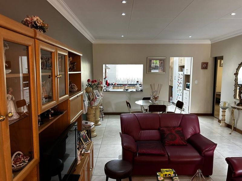 Open-plan living and dining area featuring tiled flooring, recessed ceiling lighting, and a service window connecting to the kitchen.