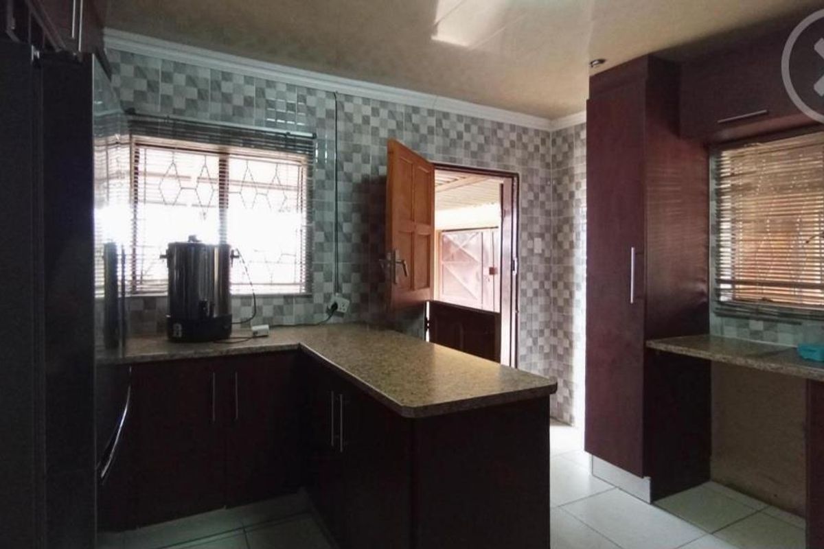A functional kitchen featuring dark wood cabinetry, granite-look countertops, and tiled walls with direct access to an exterior area.