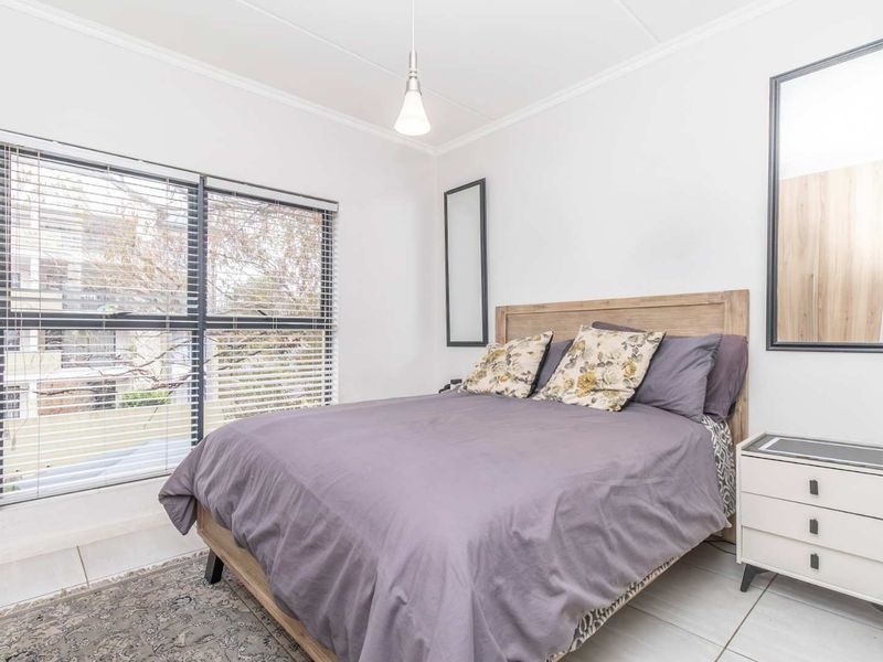A bright and well-maintained bedroom featuring tiled flooring, cove cornicing, and large windows fitted with venetian blinds.