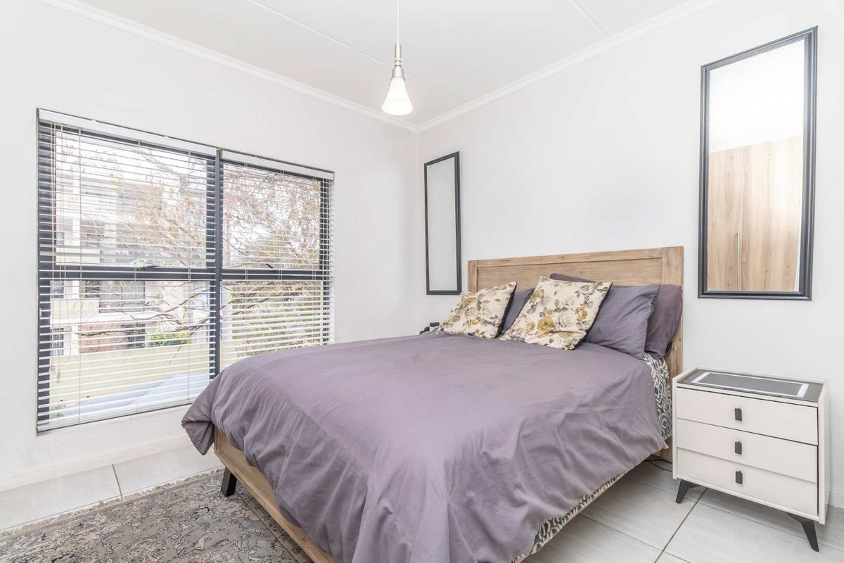A bright and well-maintained bedroom featuring tiled flooring, cove cornicing, and large windows fitted with venetian blinds.