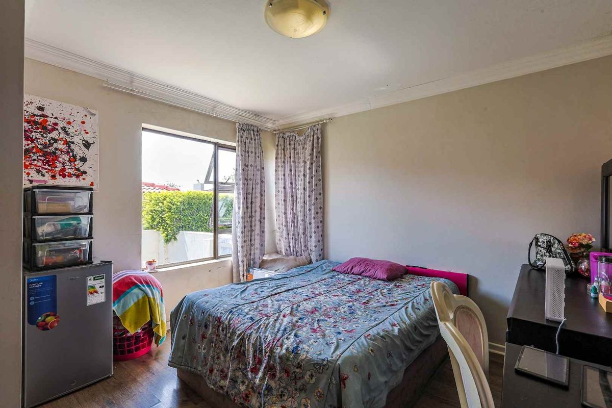 A functional bedroom featuring laminate flooring, large windows with natural light, and a central ceiling light fixture.