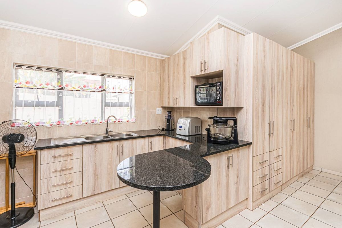A functional kitchen featuring light wood-grain cabinetry, dark granite countertops, a breakfast nook, and tiled flooring with a double sink.