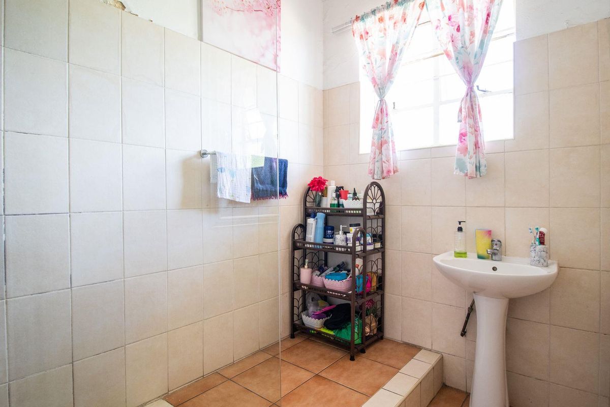 A functional bathroom featuring a pedestal sink, a glass-enclosed shower area, and neutral wall tiling.