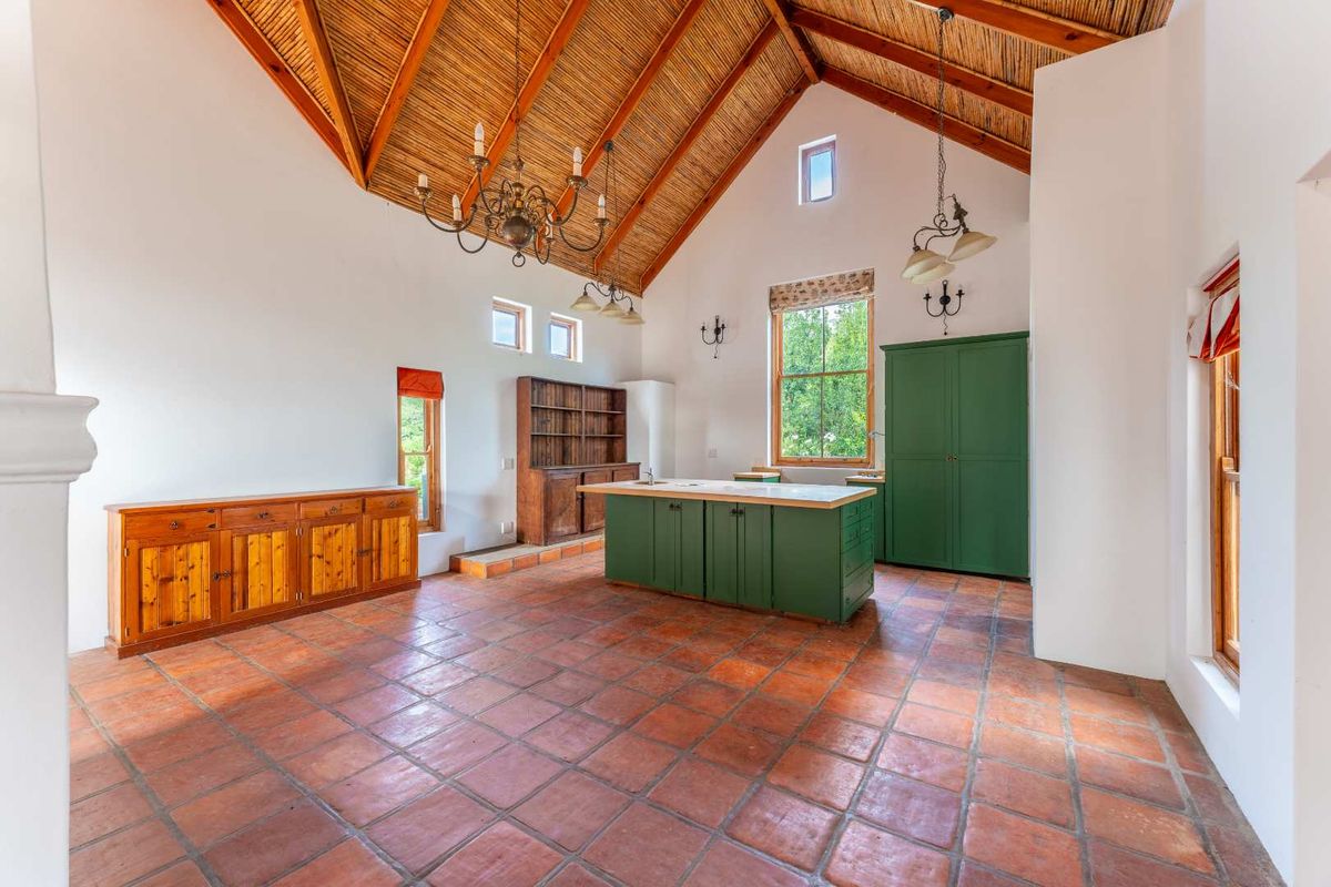Spacious kitchen featuring a high vaulted timber ceiling, terracotta tile flooring, and a central island with built-in cabinetry.