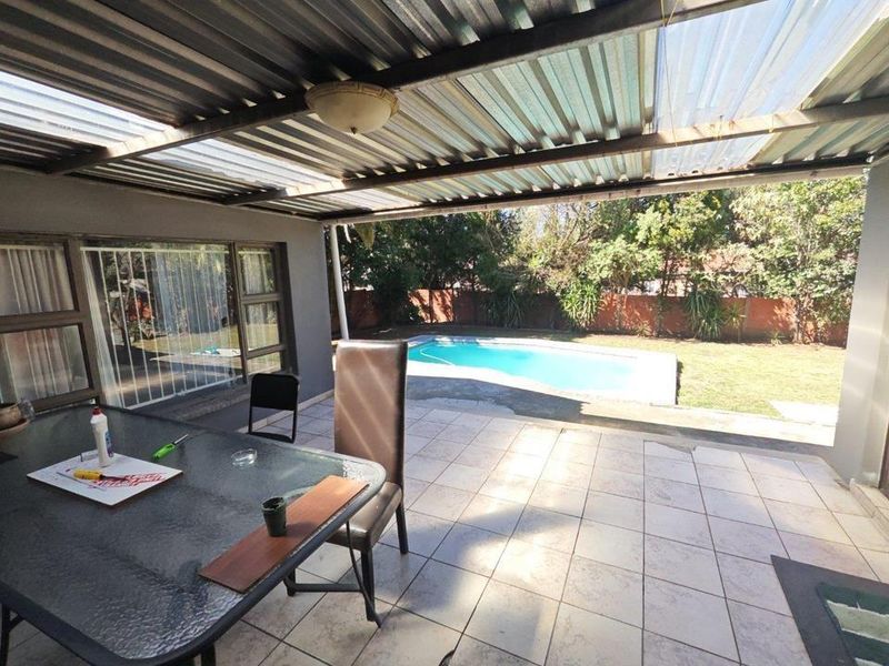 Covered outdoor patio area featuring tiled flooring and a corrugated roof, overlooking a private swimming pool and garden space.