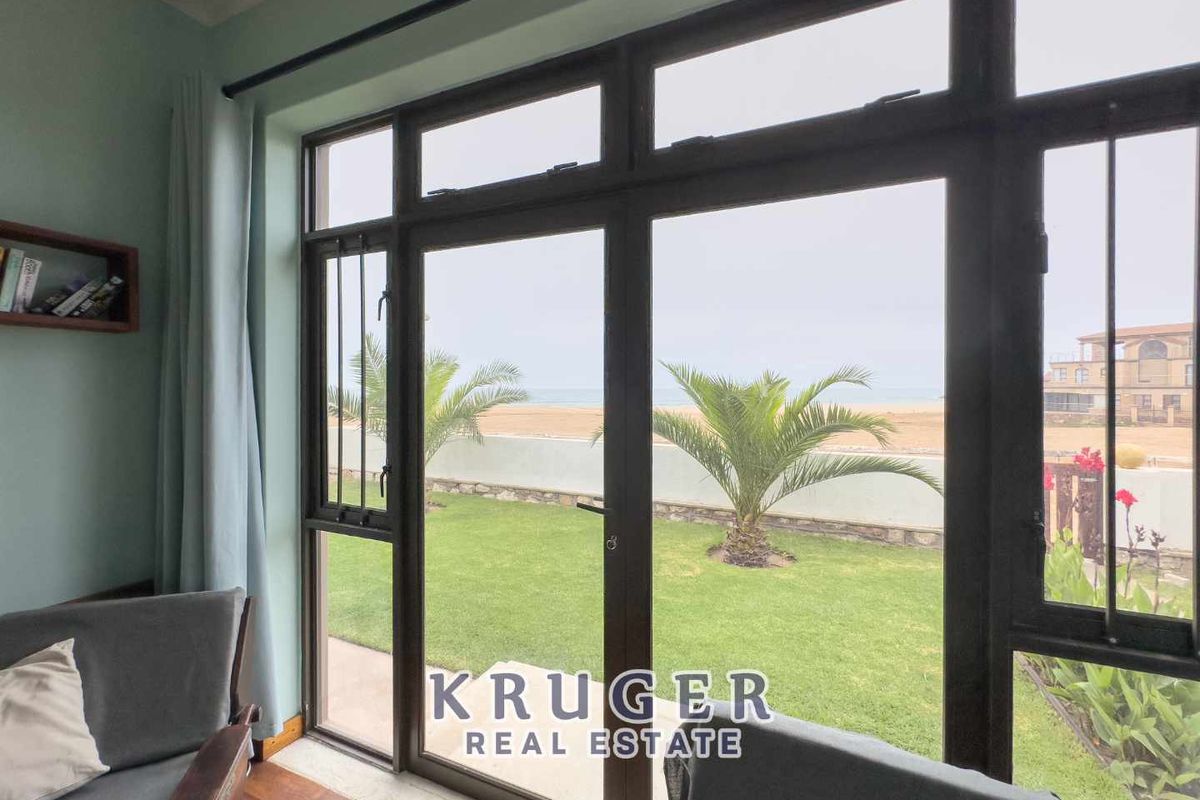 A living area featuring large dark-framed glass doors that provide direct access to a private garden and scenic coastal views.