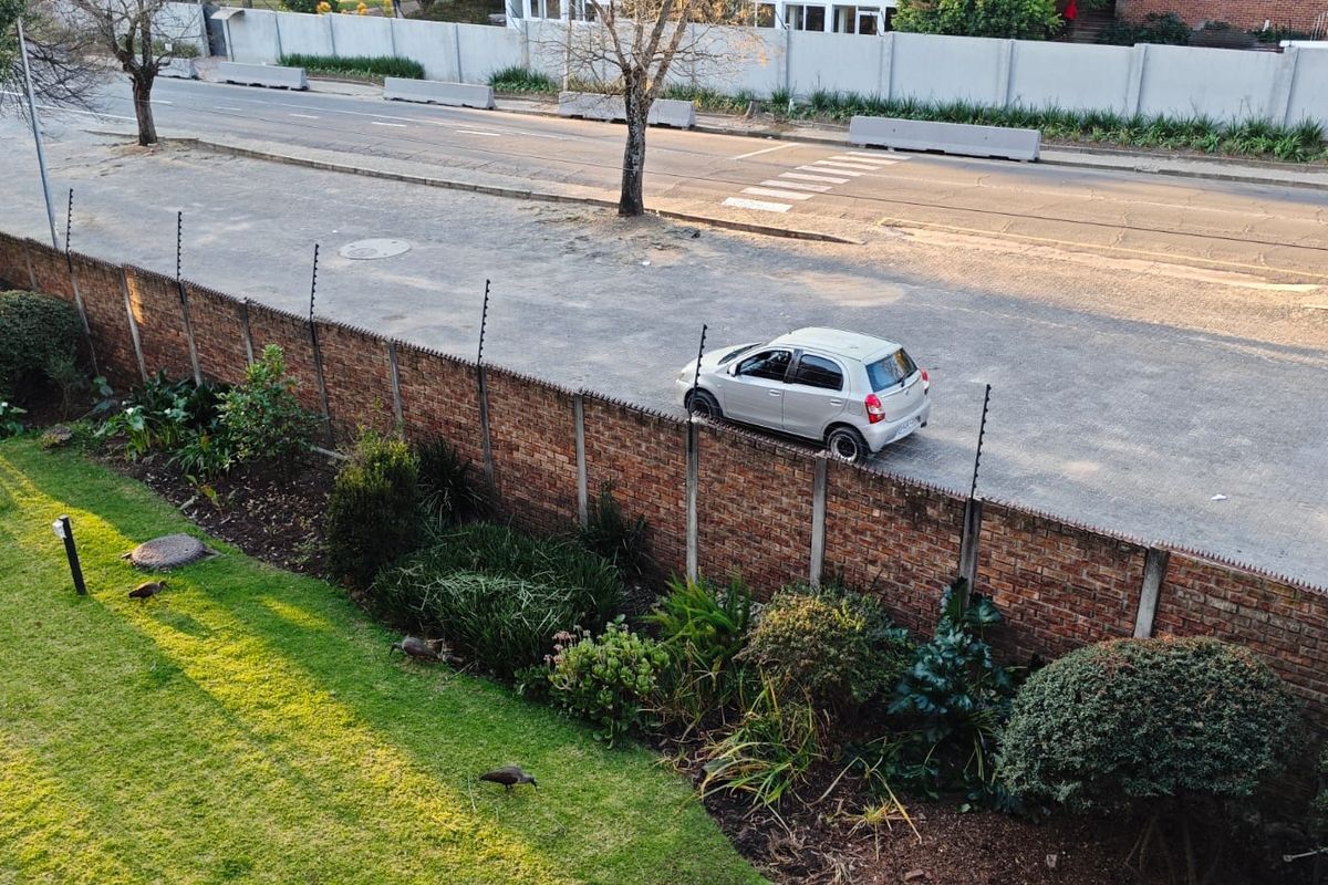 An elevated view of the property boundary featuring a brick wall with electric fencing and a well-maintained garden area adjacent to the street.
