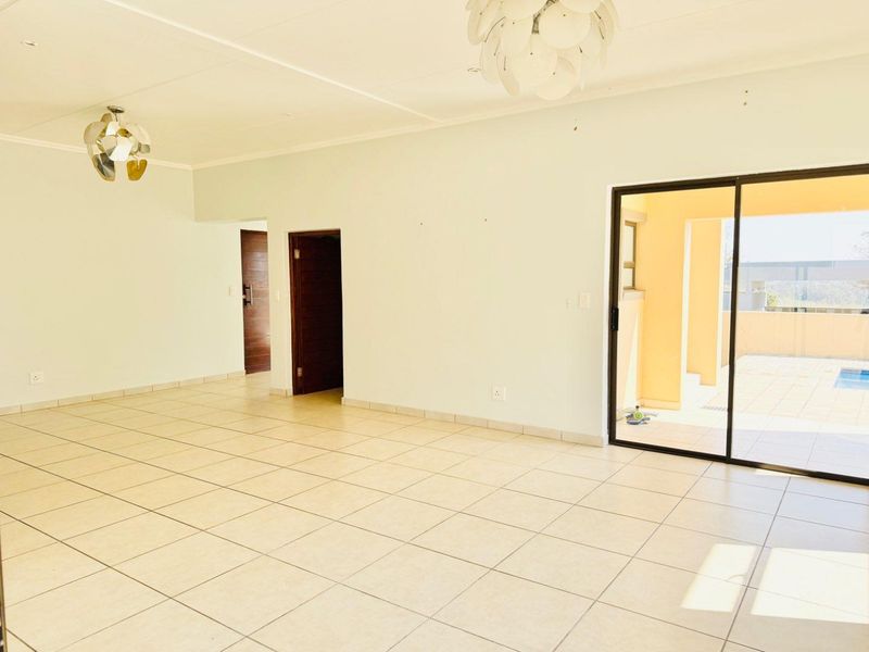 A spacious, empty living area featuring neutral tiled flooring and a large sliding glass door providing access to an outdoor patio and pool area.