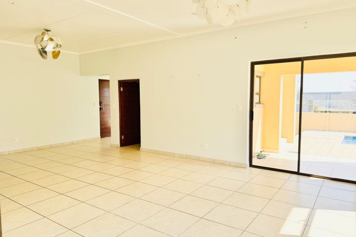 A spacious, empty living area featuring neutral tiled flooring and a large sliding glass door providing access to an outdoor patio and pool area.