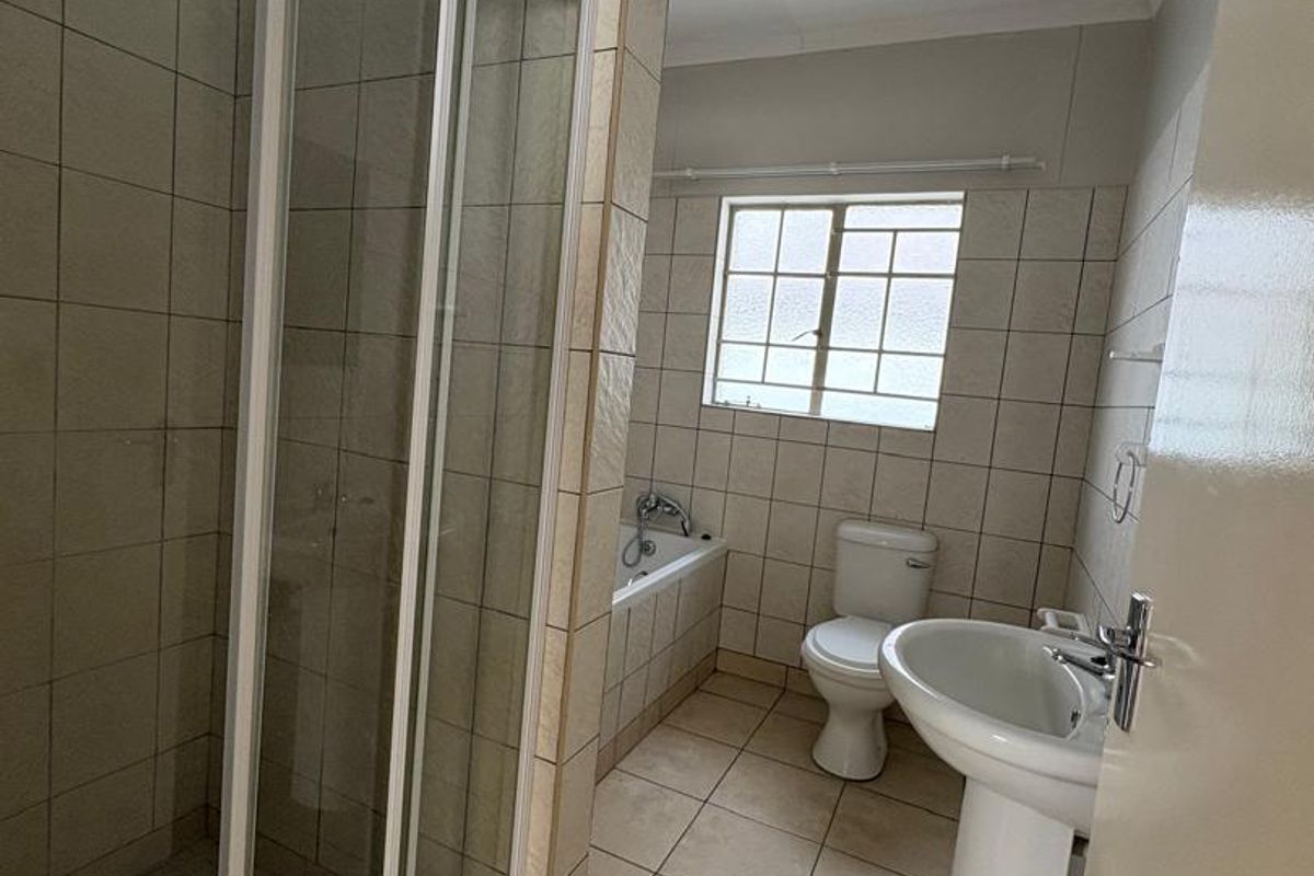 A functional bathroom featuring a glass-enclosed shower, a separate bathtub, a pedestal basin, and a toilet with neutral floor and wall tiling.