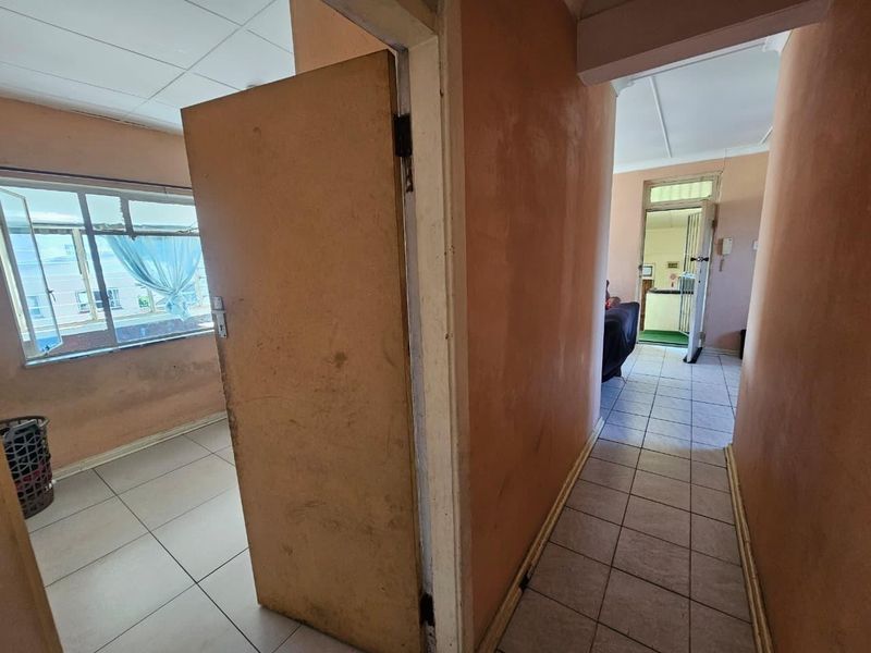 A view through a hallway connecting to an adjacent room, featuring tiled flooring and dated wall finishes in need of cosmetic attention.