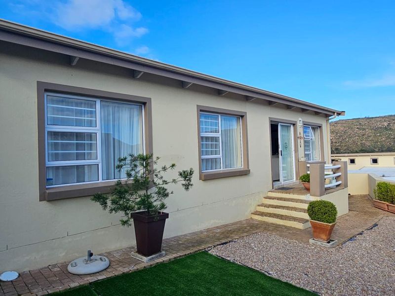 Rear exterior view of the cluster home featuring a paved walkway, concrete steps, and low-maintenance gravel landscaping with aluminium window frames.
