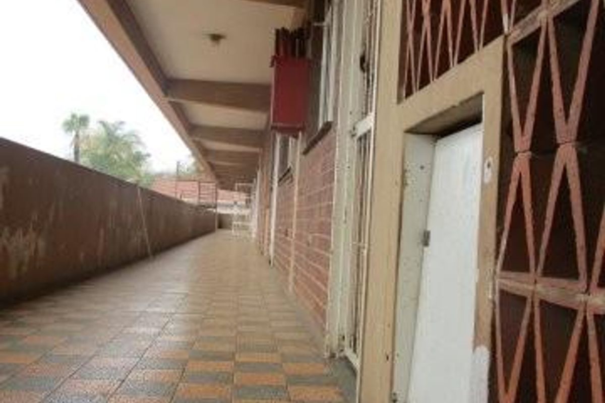 An exterior balcony or walkway featuring tiled flooring, a decorative breeze block screen, and a security gate entrance.