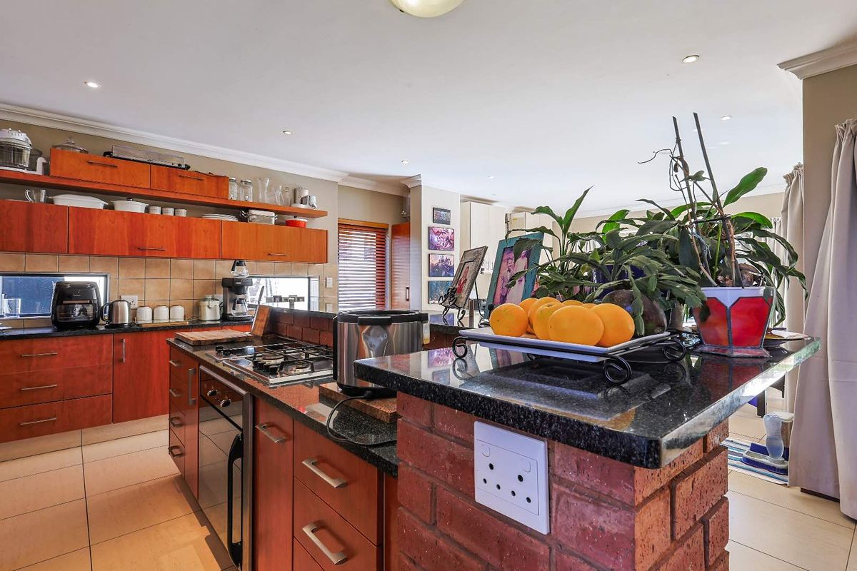 A functional kitchen featuring wood-veneer cabinetry, granite countertops, a central island with a built-in gas hob, and tiled flooring.