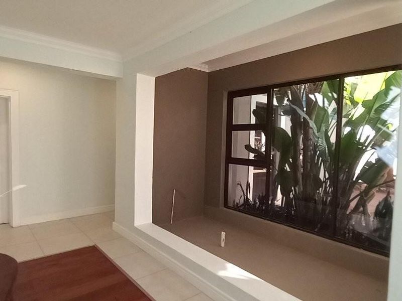 A bright, neutral living area featuring a large recessed display niche and a wide window overlooking lush greenery.