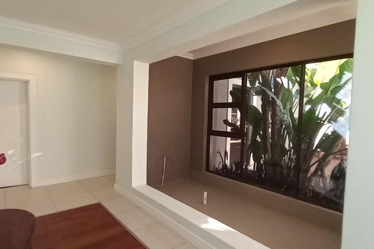 A bright, neutral living area featuring a large recessed display niche and a wide window overlooking lush greenery.