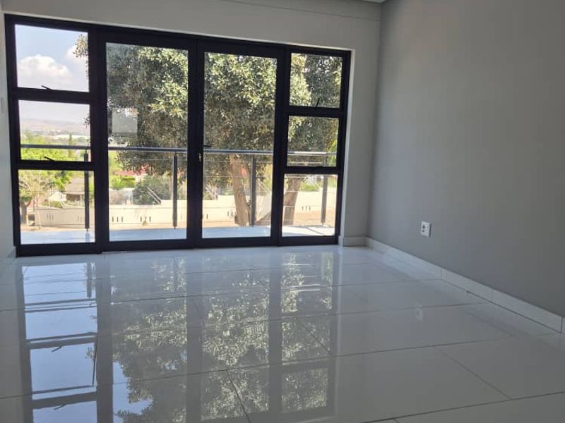 A bright, empty living room featuring large format white porcelain tiles, modern pendant lighting, and black aluminium sliding doors opening to an outdoor view.
