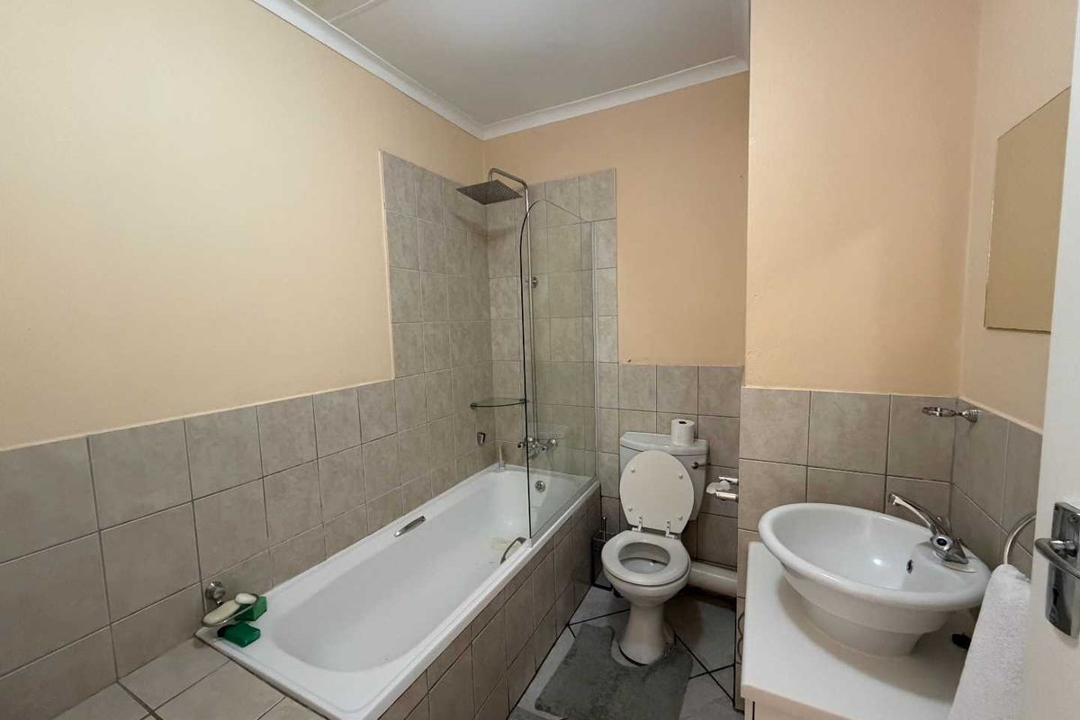 A functional bathroom featuring a bathtub with a glass shower screen, a pedestal basin, and a standard toilet with neutral wall tiling.