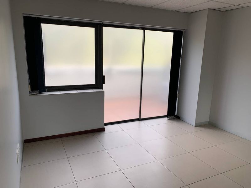 A bright, empty office space featuring large sliding glass doors with frosted privacy film, tiled flooring, and a suspended acoustic ceiling.