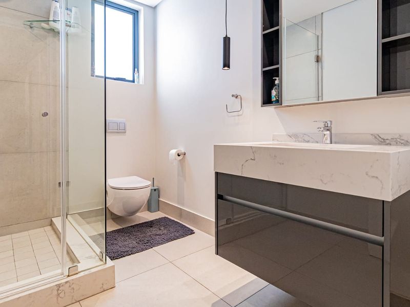 Modern bathroom featuring a wall-hung toilet, glass-enclosed shower, and a sleek vanity with a stone countertop and integrated basin.