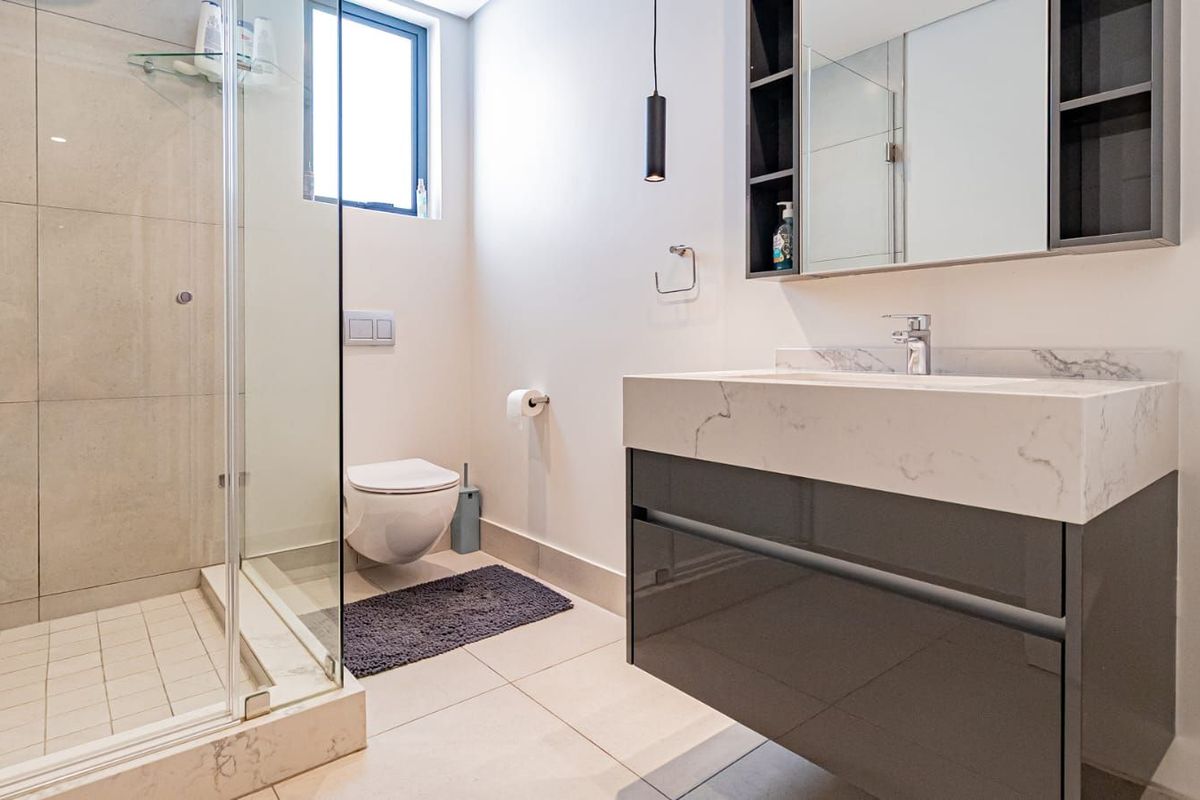 Modern bathroom featuring a wall-hung toilet, glass-enclosed shower, and a sleek vanity with a stone countertop and integrated basin.