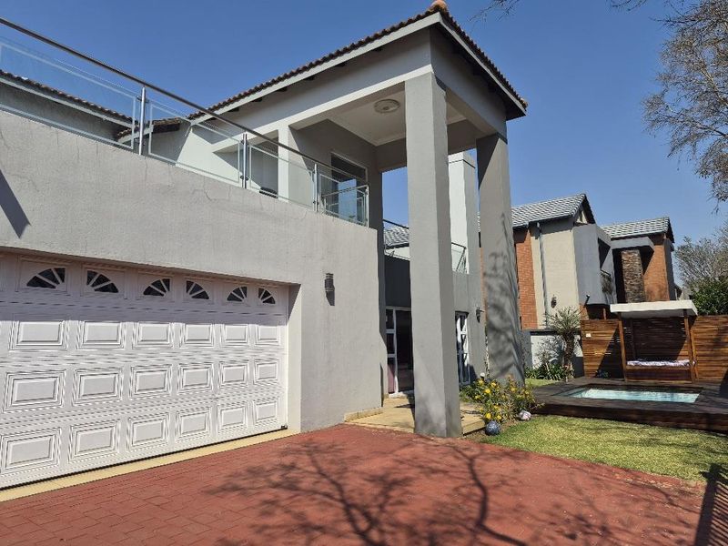Modern townhouse exterior featuring a double garage, upper-level balcony with glass balustrades, and a private garden area with a swimming pool and wooden deck.