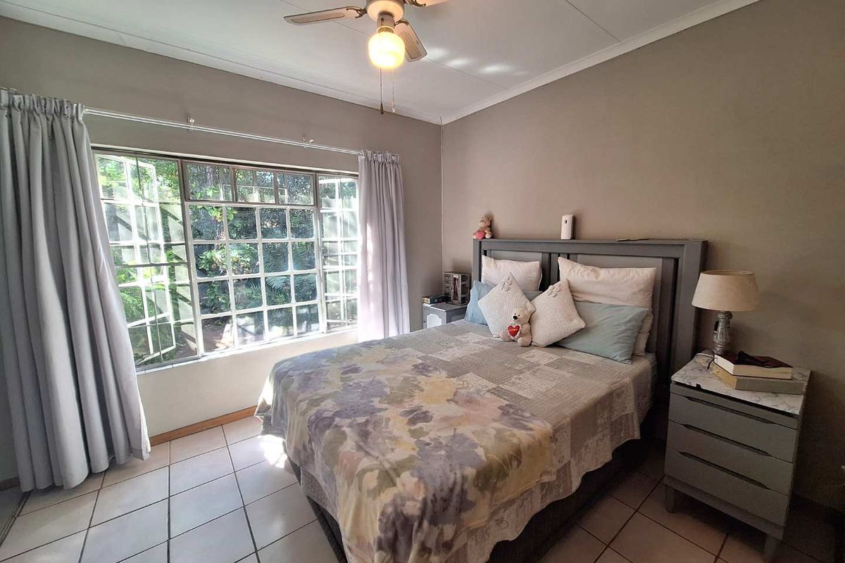 A bedroom featuring tiled flooring, a ceiling fan, and a large window overlooking the garden.