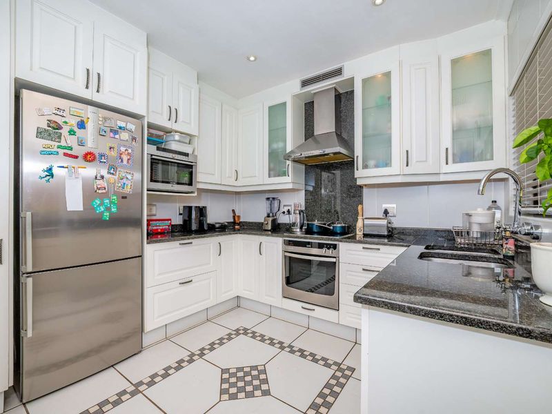 A well-maintained kitchen featuring white cabinetry, granite countertops, stainless steel appliances, and decorative tiled flooring.