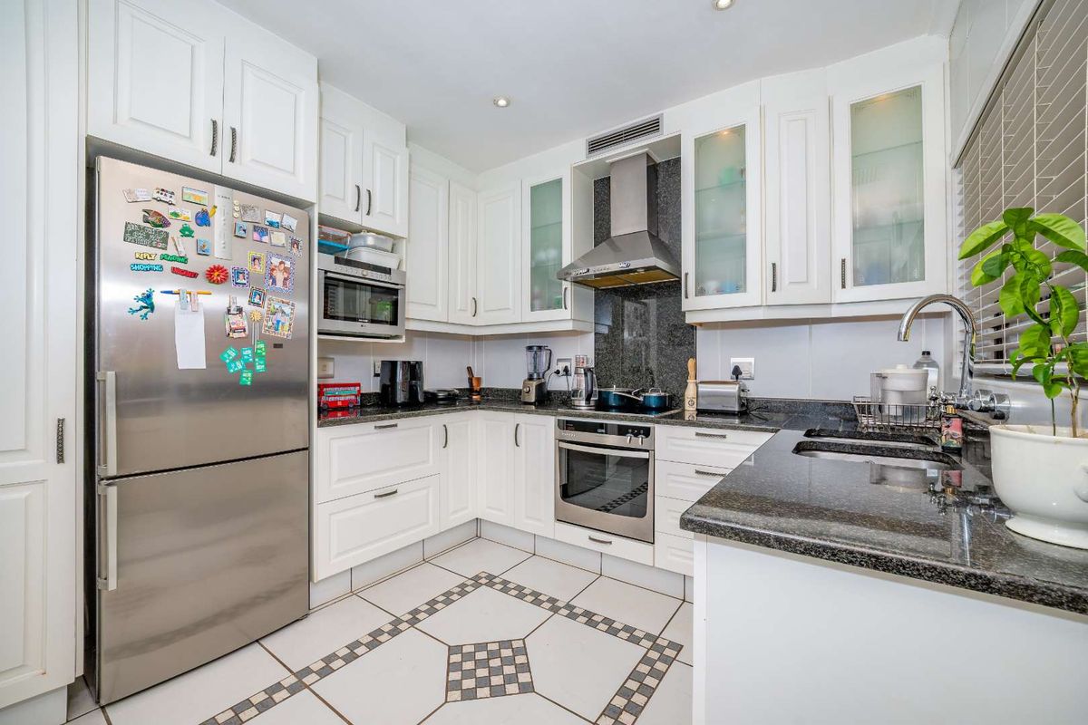 A well-maintained kitchen featuring white cabinetry, granite countertops, stainless steel appliances, and decorative tiled flooring.