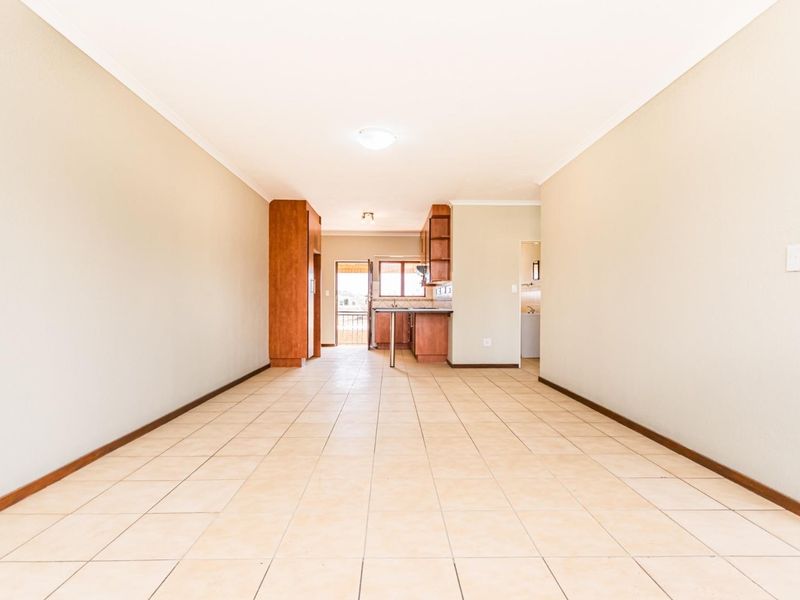 An open-plan living and kitchen area featuring neutral walls, tiled flooring, and built-in wooden cabinetry, offering a clean and versatile space.