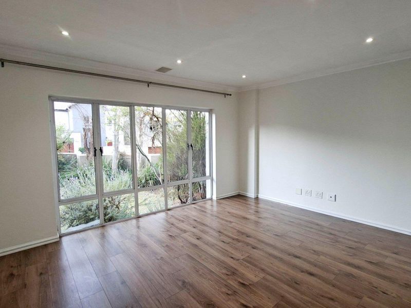 A bright and spacious living area featuring modern laminate flooring, recessed downlighting, and a large window overlooking the garden.
