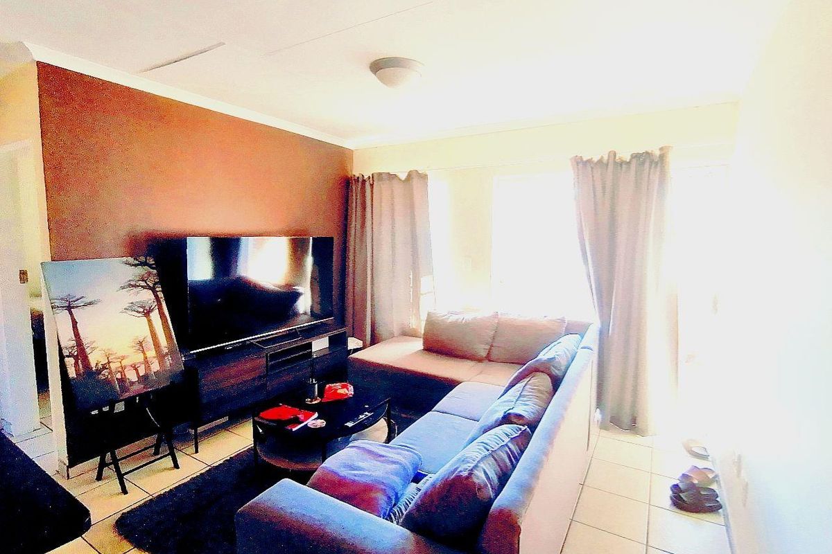 A living room featuring tiled flooring and a large window with curtains, providing natural light to the space.