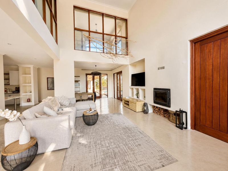 Spacious open-plan living area featuring double volume ceilings, polished concrete floors, a built-in fireplace, and large windows providing abundant natural light.