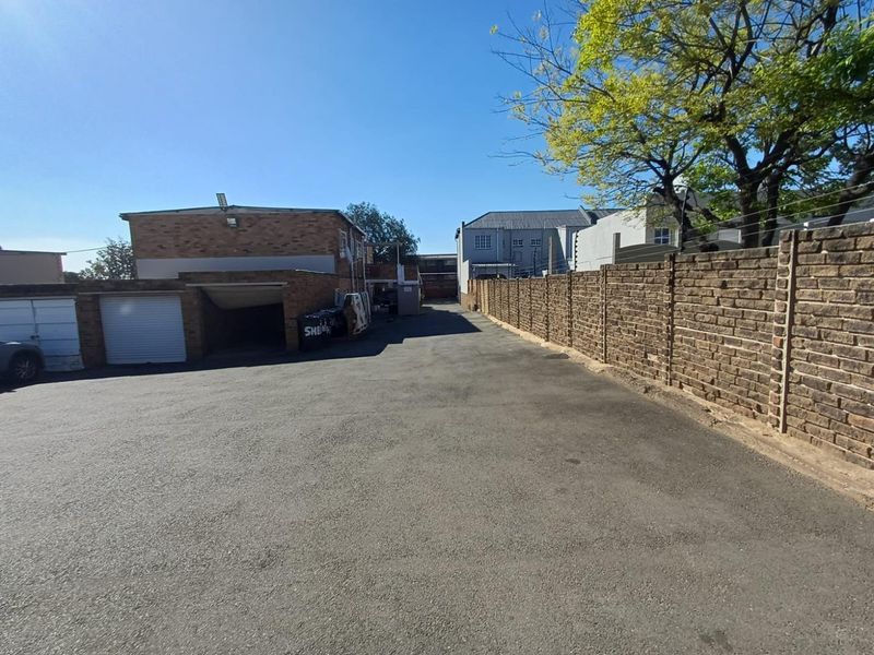 Rear exterior view of the apartment complex featuring an asphalt driveway, brick boundary wall, and secure garage access.