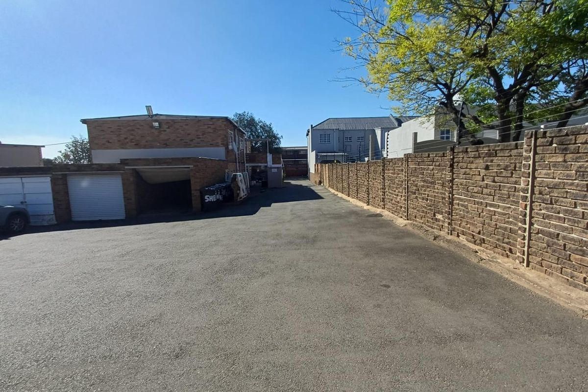 Rear exterior view of the apartment complex featuring an asphalt driveway, brick boundary wall, and secure garage access.