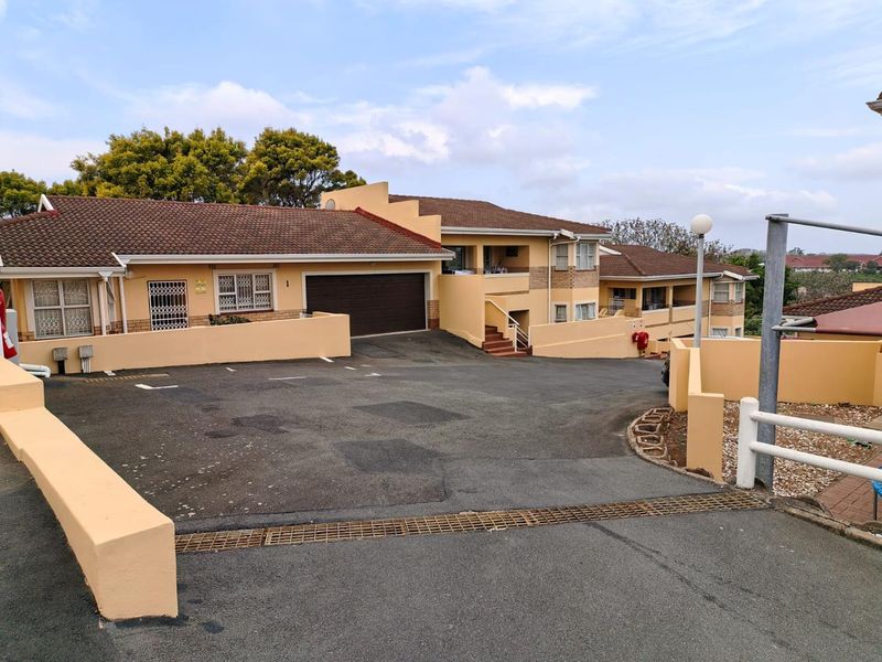 Front exterior view of a townhouse complex featuring an asphalt driveway, double garage, and tiled roofing with perimeter boundary walls.