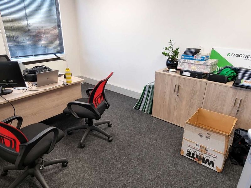 A functional office space featuring carpeted flooring, built-in storage cabinetry, and large windows with venetian blinds for natural light.
