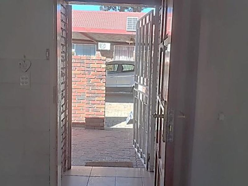 An entry point featuring a security gate, tiled flooring, and a view leading out to a paved courtyard area.
