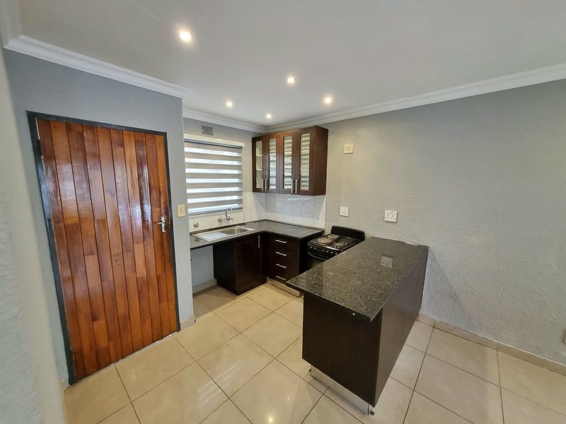 A clean, functional kitchen featuring dark wood cabinetry, granite countertops, tiled flooring, and a breakfast nook, offering a neutral and well-maintained space.