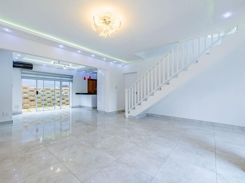 Spacious open-plan living area featuring polished porcelain tiles, a modern staircase, recessed lighting, and a built-in bar area with access to the rear exterior.