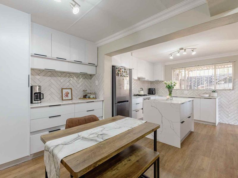 Modern kitchen featuring white cabinetry, a central quartz island, herringbone tile backsplash, and durable laminate flooring in an open-plan layout.