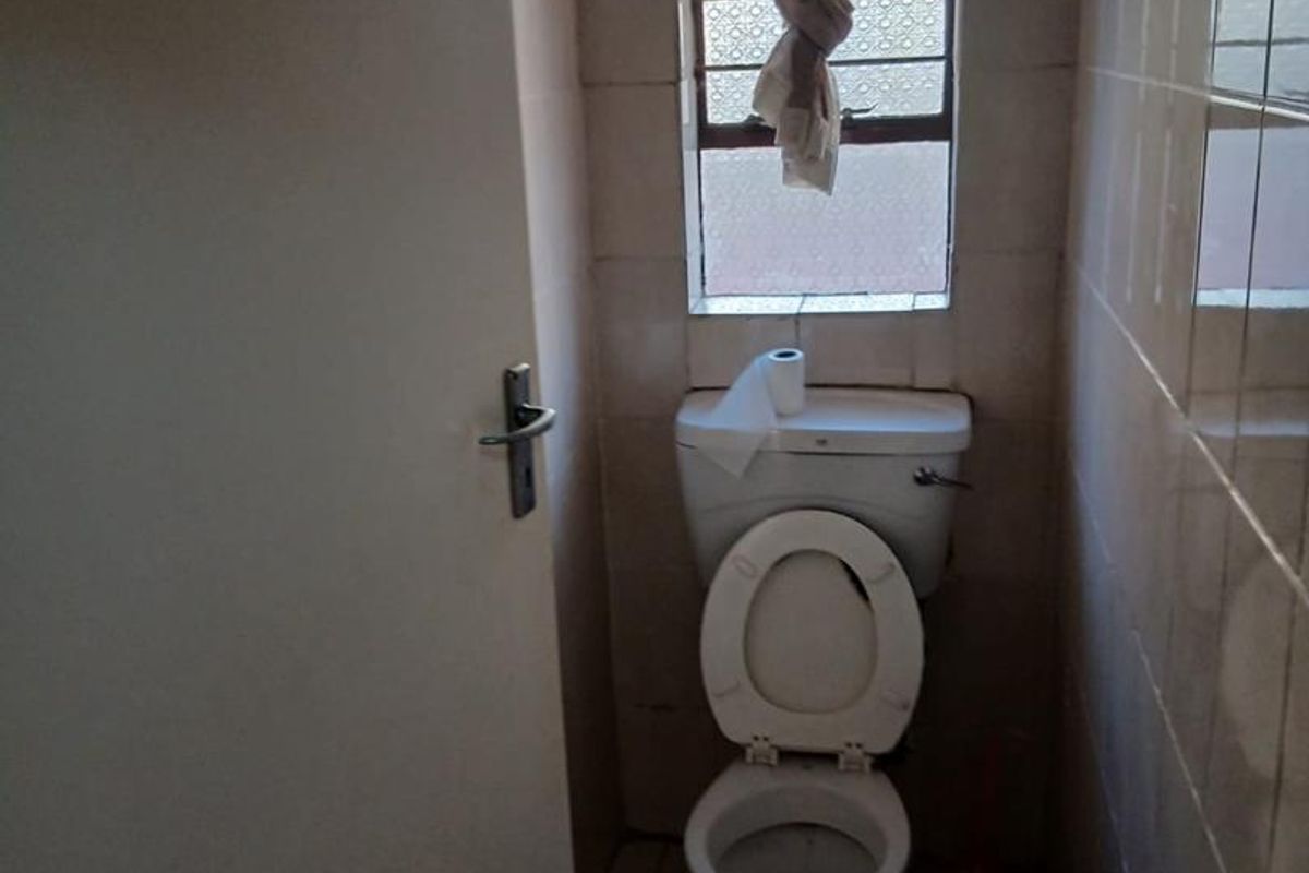 A compact, functional bathroom featuring tiled walls and flooring, equipped with a standard toilet and a window with security bars.
