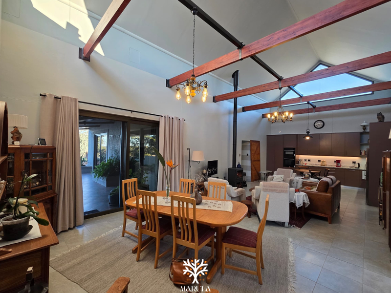 Spacious open-plan living and dining area featuring high vaulted ceilings with exposed timber beams, a wood-burning fireplace, and a modern kitchen.