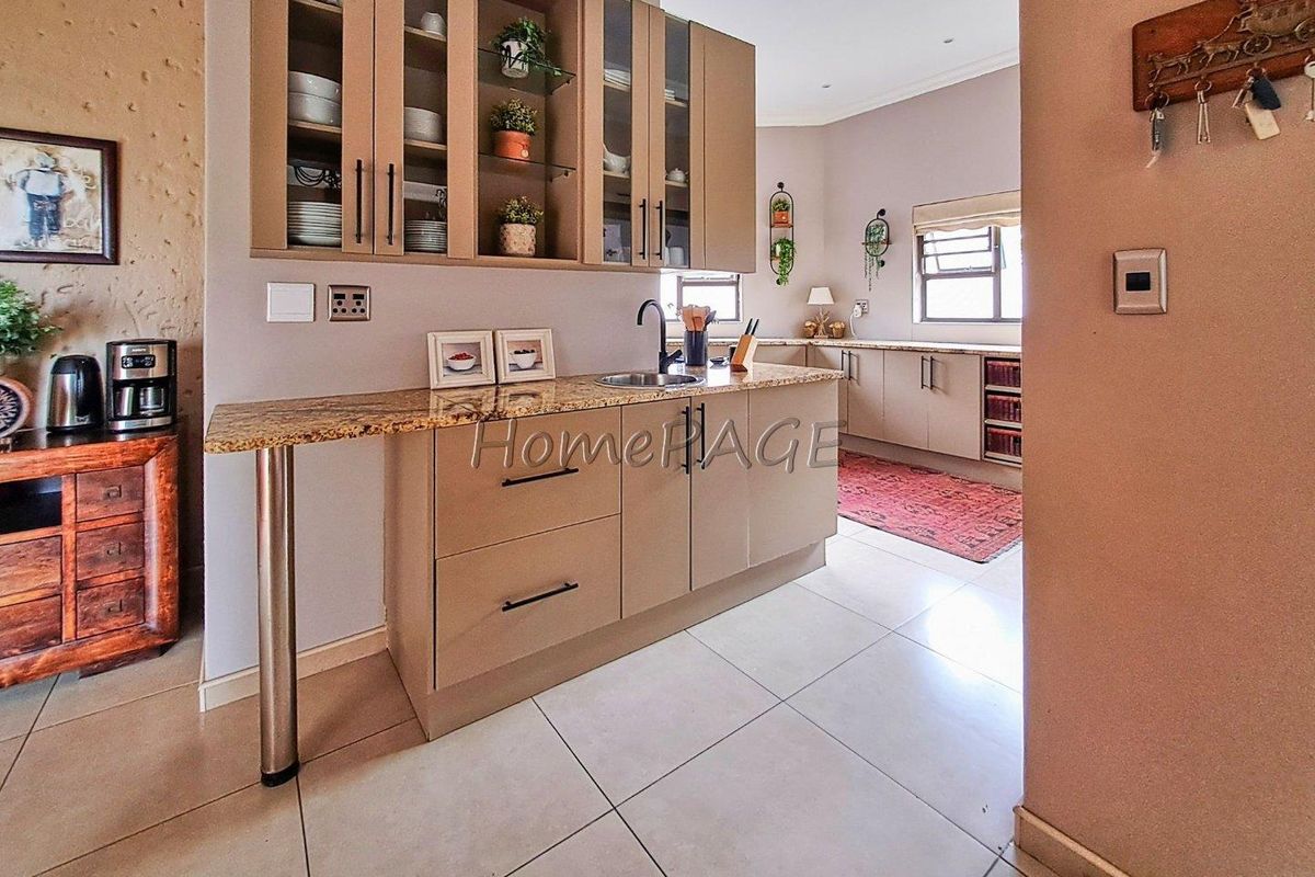 A functional kitchen featuring light-toned cabinetry, granite countertops, a stainless steel sink, and tiled flooring, offering a clean and organized workspace.