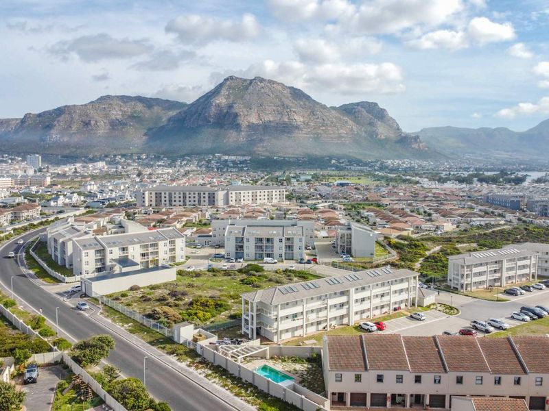 Aerial view of a residential apartment complex featuring paved parking, a swimming pool, and scenic mountain views in the background.