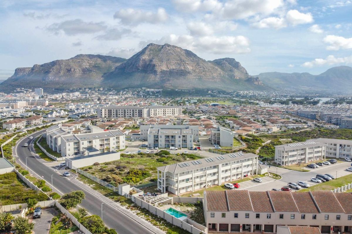 Aerial view of a residential apartment complex featuring paved parking, a swimming pool, and scenic mountain views in the background.