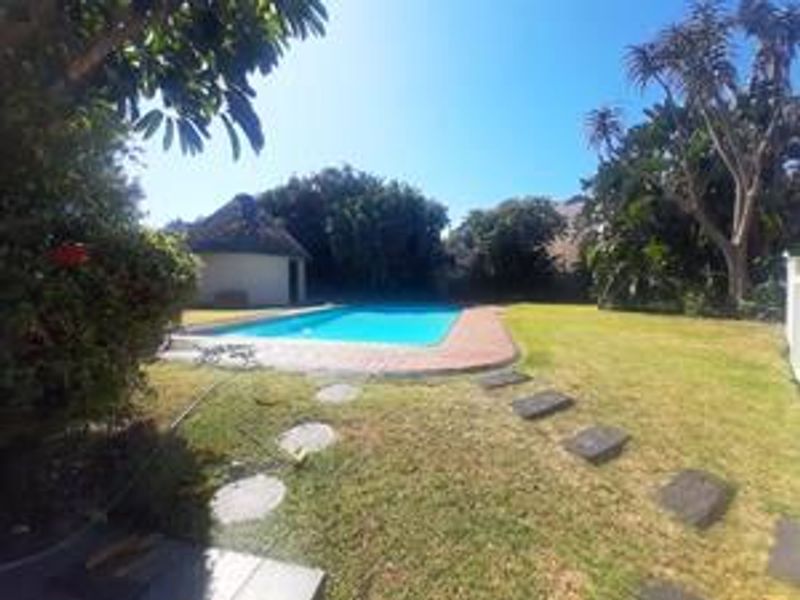 A private outdoor pool area featuring a swimming pool with paved surround, a thatched lapa, and a well-maintained garden lawn.