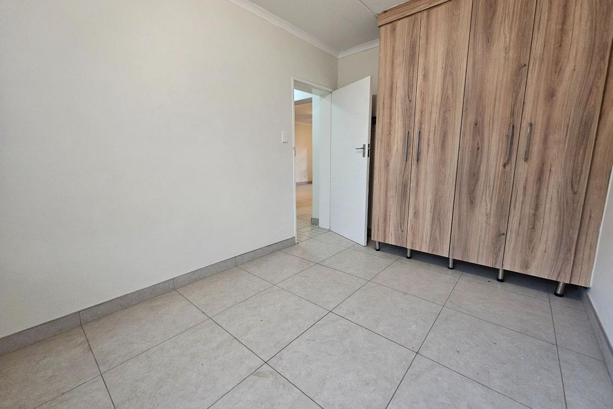 A clean, empty bedroom featuring neutral floor tiles and modern built-in wooden cupboards, offering a versatile space ready for personalization.