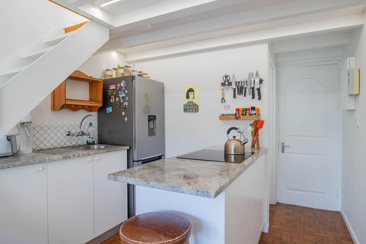 Compact kitchen featuring granite countertops, built-in cabinetry, an integrated cooktop, and a stainless steel sink, situated beneath a staircase.